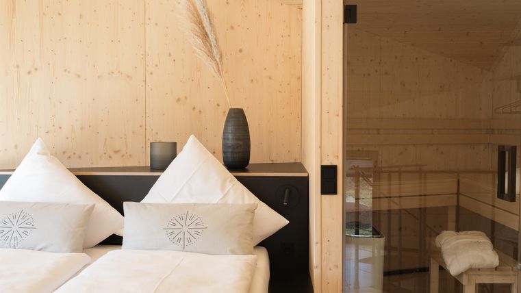 Ein modernes Schlafzimmer mit zwei Betten und eleganter Holzverkleidung. Im Hintergrund befindet sich eine Sauna mit Bänken.