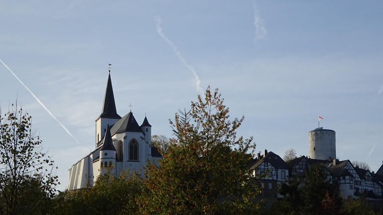 Ein malerisches Dorf mit einer Kirche und einem Aussichtsturm, umgeben von Bäumen. Der Himmel ist klar und die Atmosphäre ist ruhig.