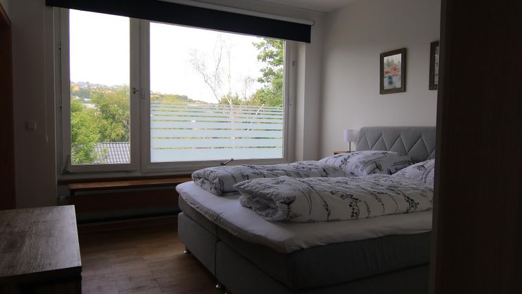 Ein helles Schlafzimmer mit einem großen Fenster und einem Blick ins Grüne. Das Bett ist mit gemütlichen Bettwäsche und Kissen ausgestattet.