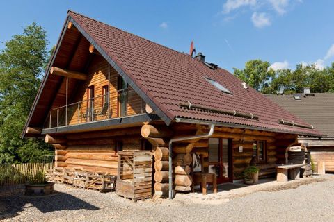 Ein Holzhaus mit einem steilen Dach und großen Fenstern. Es befindet sich in einer ruhigen ländlichen Umgebung.