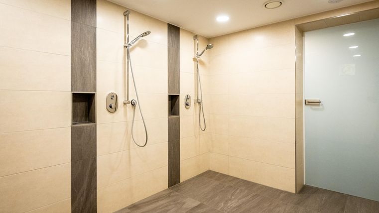 Ein modernes Badezimmer mit zwei Duschbereichen und hellem Fliesenboden. Die Wände sind in neutralen Farben gehalten und es gibt eine transparente Glasduschtür.