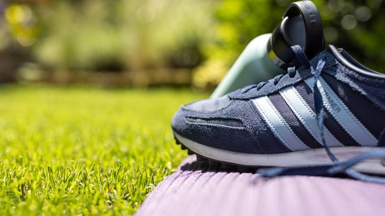 Ein Sport Schuh liegt auf einer Yogamatte im Gras. Im Hintergrund ist ein Fitnessgerät zu sehen.