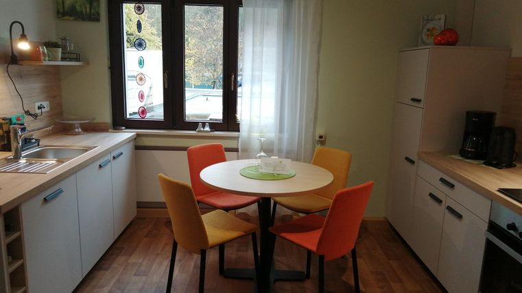 Eine moderne Küche mit einem runden Tisch und bunten Stühlen. Helle Farbgestaltung und große Fenster sorgen für ein einladendes Ambiente.