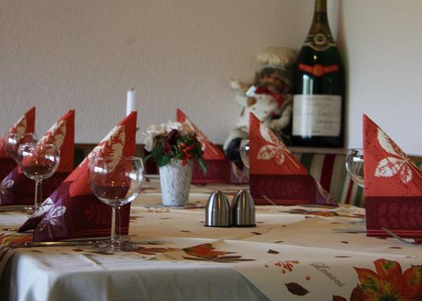 Ein schön gedeckter Tisch mit roten Servietten und Gläsern. Im Hintergrund steht eine Flasche Champagner und eine kleine Blumendekoration.