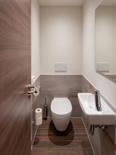 Ein modernes Badezimmer mit einer Toilette und einem kleinen Waschbecken. Die Wände sind hell und der Boden ist aus Holz.