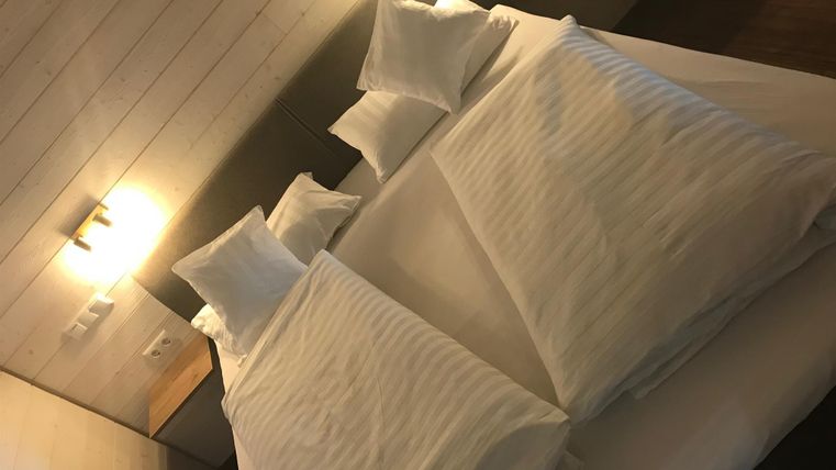 Ein modernes Schlafzimmer mit einem großen Bett, das mit weißen Kissen und Bettwäsche ausgestattet ist. Sanftes Licht beleuchtet den Raum und schafft eine gemütliche Atmosphäre.