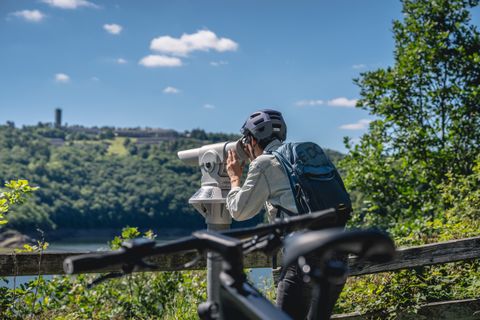 Person mit Helm schaut durch ein Fernglas auf einer Vogelbeobachtungsstation, im Hintergrund Vogelsang IP.