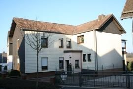 Ein modernes Wohnhaus mit einem schrägen Dach. Die Fassade ist in verschiedenen Farben gestaltet und hat große Fenster.