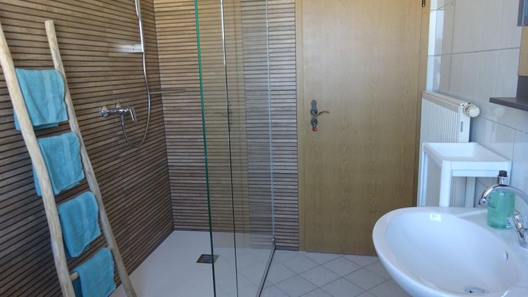 Ein modernes Badezimmer mit einer gläsernen Dusche und einem Waschbecken. Handtücher sind ordentlich auf einem Holzregal platziert.