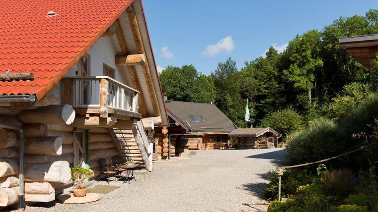 Ein charmantes Holzhaus mit rotem Dach und einem einladenden Außenbereich. Die Umgebung ist grün und bietet eine ruhige Atmosphäre.