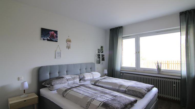 Ein helles Schlafzimmer mit einem Doppelbett und zwei Nachttischen. Große Fenster lassen viel natürliches Licht herein.