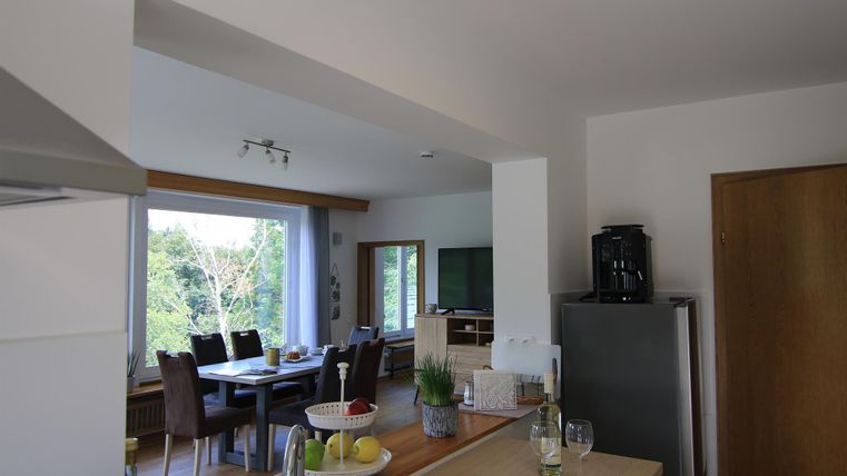 Eine moderne Küche mit einem offenen Wohnbereich. Es gibt einen Essbereich mit einem großen Tisch und Stühlen sowie eine große Fensterfront, die viel Tageslicht hereinlässt.