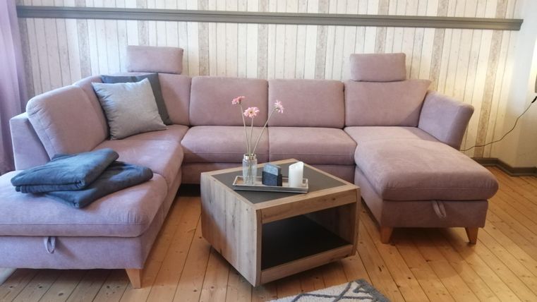 Ein modernes Wohnzimmer mit einem großen, lila Sofa und einem Holztisch in der Mitte. Auf dem Tisch stehen eine Vase mit Blumen und einige dekorative Gegenstände.