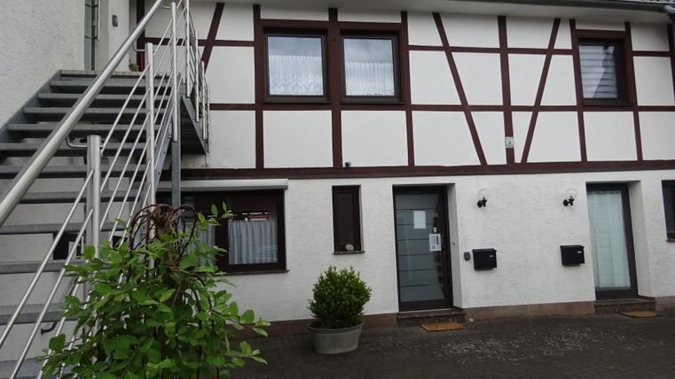 Ein modernes Gebäude mit Fachwerk-Elementen und einer Außentreppe. Es gibt mehrere Eingänge und Pflanzen in Töpfen.