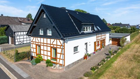 Ein modernes Haus mit traditionellem Fachwerkstil und einem schwarzen Dach. Der Garten ist ordentlich und mit bunten Blumen bepflanzt.