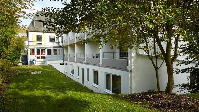 Ein modernes Gebäude mit mehreren Balkonen und einer gepflegten Grünfläche. Bäume umgeben den Garten und verleihen der Umgebung eine ruhige Atmosphäre.