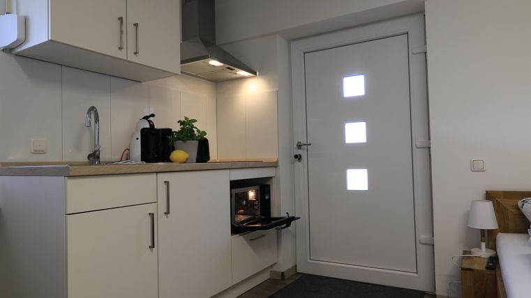 Eine moderne Küche mit weißen Schränken und einem Ofen. Die Tür ist weiß und hat quadratische Fenster.