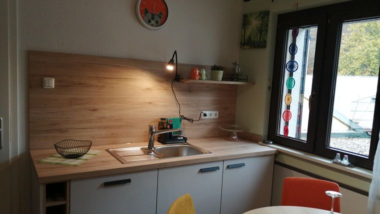 Eine moderne Küche mit Holzregalen und einem großen Fenster. Der Tisch ist mit bunten Stühlen und einem kleinen Dekorationsartikel gedeckt.