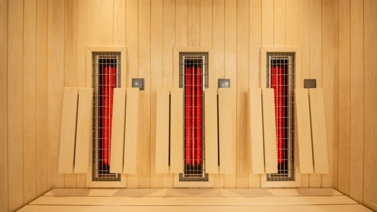Ein moderner Wellnessbereich mit drei Infrarotkabinen. Die Wände sind aus hellem Holz und die Heizpanel strahlen rotes Licht aus.