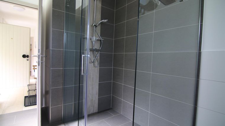 Ein modernes Duschbad mit großen Glaswänden und grauen Fliesen. Das Raumdesign ist schlicht und elegant.