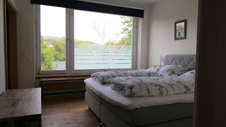 Ein gemütliches Schlafzimmer mit einem großen Fenster und einem Blick ins Grüne. Das Bett ist mit weißen Bettdecken und Kissen ausgestattet.