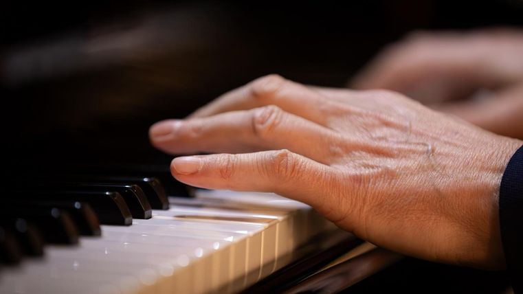 Eine Hand spielt Klavier. Die Tasten sind gut sichtbar, während die Finger in Bewegung sind.