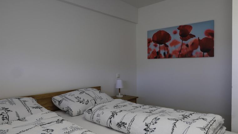 Ein gemütliches Schlafzimmer mit einem Doppelbett und floralen Bettbezügen. An der Wand hängt ein Bild mit roten Mohnblumen auf blauem Hintergrund.