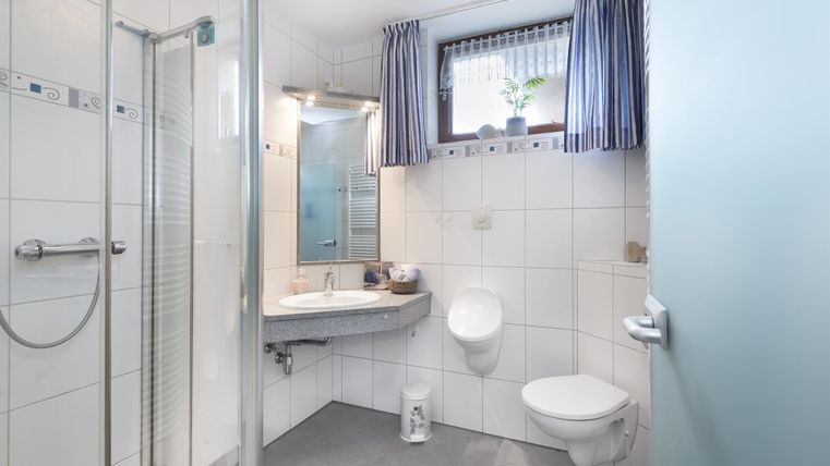 Ein modernes Badezimmer mit Dusche, Waschbecken und Toilette. Die Wände sind gefliest und das Fenster hat einen Blick nach draußen.