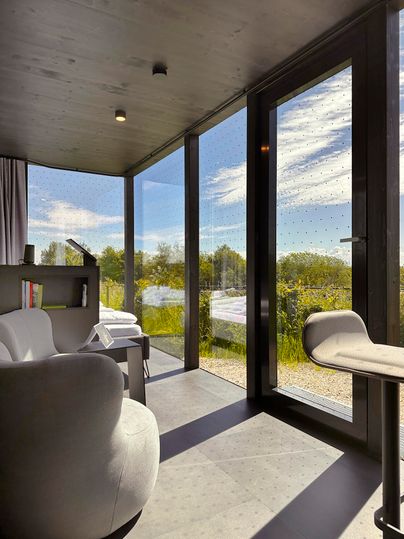 Ein modernes Zimmer mit großen Fenstern und Blick auf die Natur. Innen gibt es bequeme Möbel und eine helle, einladende Atmosphäre.
