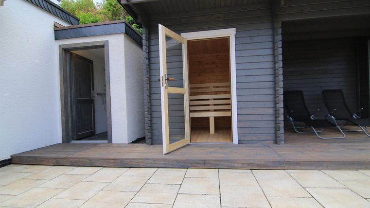 Ein gemütlicher Außenbereich mit einer Sauna und Liegen. Die Terrassentüren sind geöffnet und laden zum Entspannen ein.