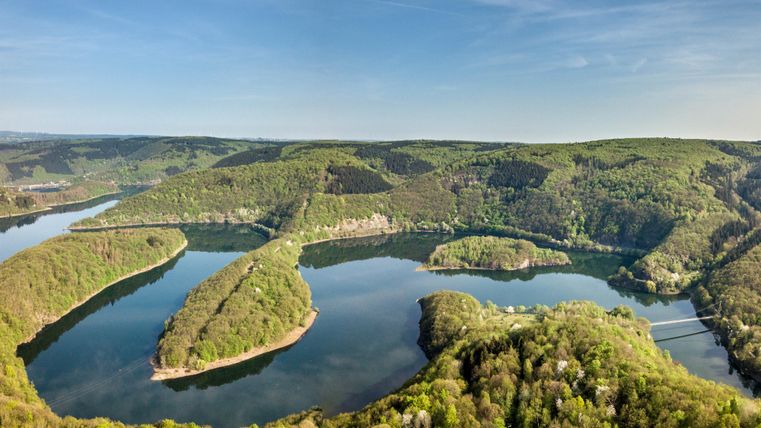 Eine atemberaubende Landschaft mit einem gewundenen Fluss, umgeben von grünen Wäldern und Hügeln. Der Himmel ist klar und die Natur wirkt friedlich.