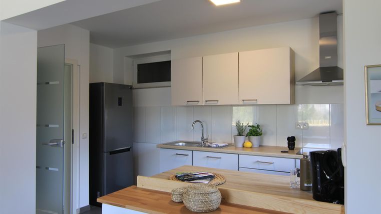 Eine moderne Küche mit weißen Schränken und einem Holzarbeitsplatte. Es gibt eine Spüle, einen Kühlschrank und einige Pflanzen für eine angenehme Atmosphäre.