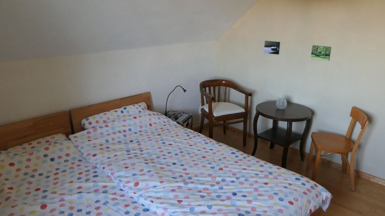 Ein gemütliches Schlafzimmer mit einem Doppelbett und bunten Bettbezügen. Es gibt einen kleinen Tisch und zwei Stühle sowie Bilder an der Wand.