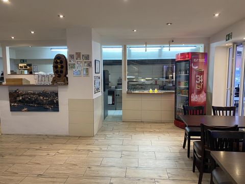 A cozy restaurant with wooden tables and chairs.
Pictures hang on the wall, and there is a refrigerator for drinks.