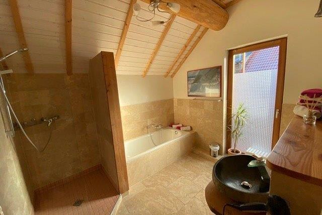Ein modernes Badezimmer mit Holzrahmen und Fliesen. Es gibt eine Dusche, eine Badewanne und eine Pflanze neben dem Fenster.