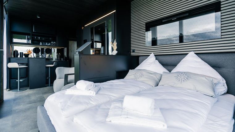 Ein modernes Schlafzimmer mit einem großen Bett und eleganter Dekoration. Im Hintergrund ist eine offene Küchenzeile und ein stilvoller Wohnbereich zu sehen.