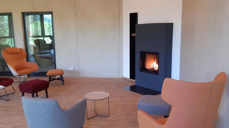 Ein modernes Wohnzimmer mit gemütlichen Sesseln in verschiedenen Farben. Im Raum befindet sich ein moderner Kamin, der eine warme Atmosphäre schafft.