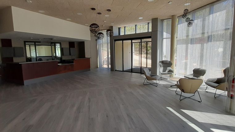 Ein moderner Empfangsbereich mit großen Fenstern und hellem Holzfußboden. Es gibt gemütliche Sitzmöglichkeiten und eine einladende Atmosphäre.