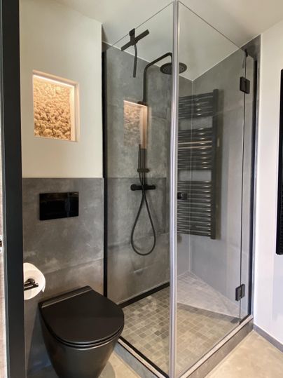 Ein modernes Badezimmer mit einer Duschkabine aus Glas und einem eleganten schwarzen WC. Die Wände sind in neutralen, modernen Farben gehalten.