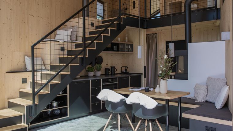 Eine moderne Wohnung mit Holzverkleidung und einer offenen Treppe. Der Bereich enthält eine Küche, einen Essplatz und gemütliche Sitzgelegenheiten.