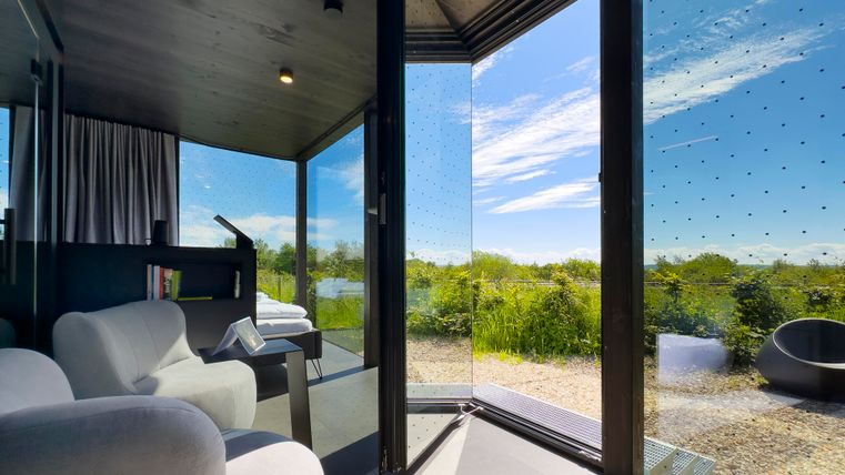 Ein modernes, lichtdurchflutetes Zimmer mit großen Fensterfronten und einem Blick ins Grüne. Die Möbel wirken elegant und einladend.