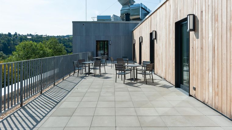 Eine moderne Terrasse mit Tischen und Stühlen. Die Umgebung ist grün und der Himmel ist klar.