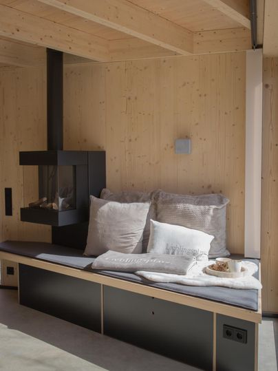 Ein moderner Wohnraum mit einer gemütlichen Sitzbank und einem Kamin. Die Wände sind aus Holz, was eine warme Atmosphäre schafft.